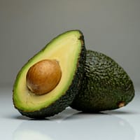 Close-up of a halved avocado with seed, showcasing vibrant colors on a reflective white background.
